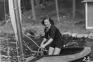 A black and white photo of a woman in a boat close to shore