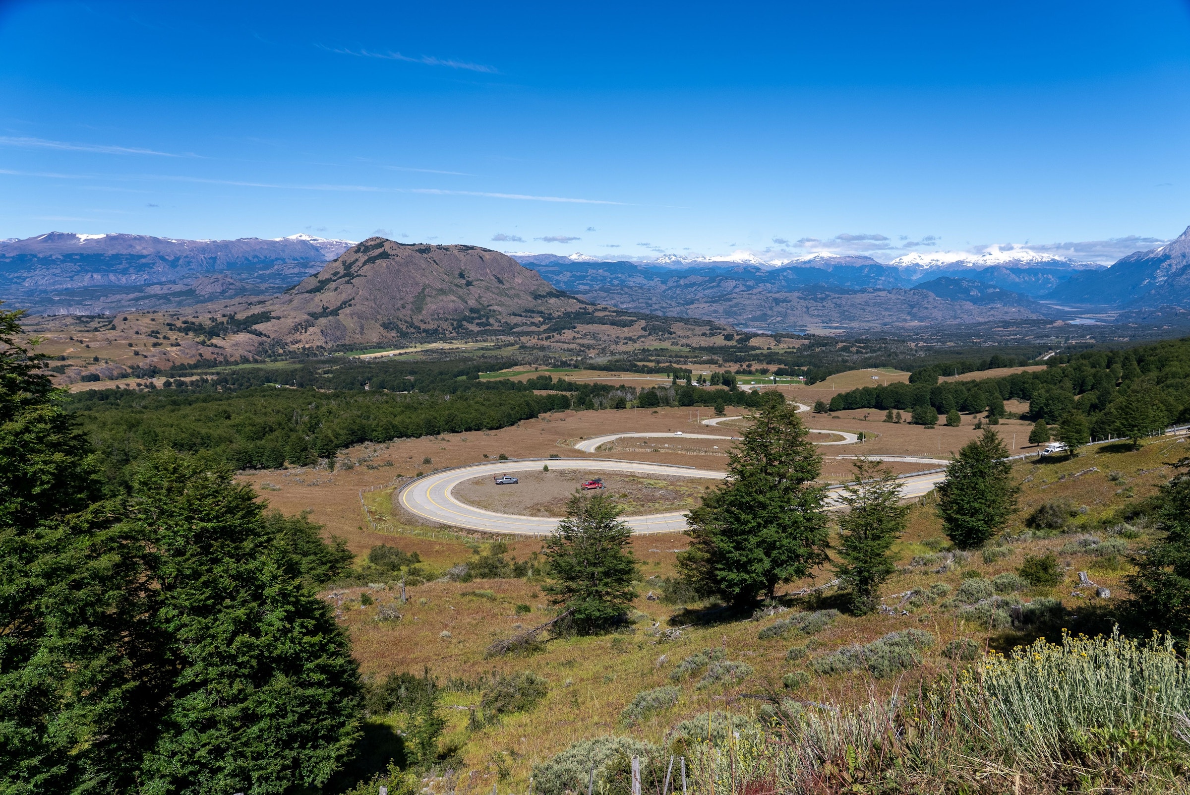 Road winding through a wide mountain valley under a blue sky