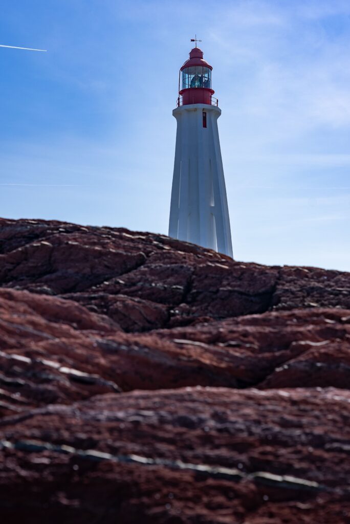 White lighthouse on a red rock outcrop under a clear sky