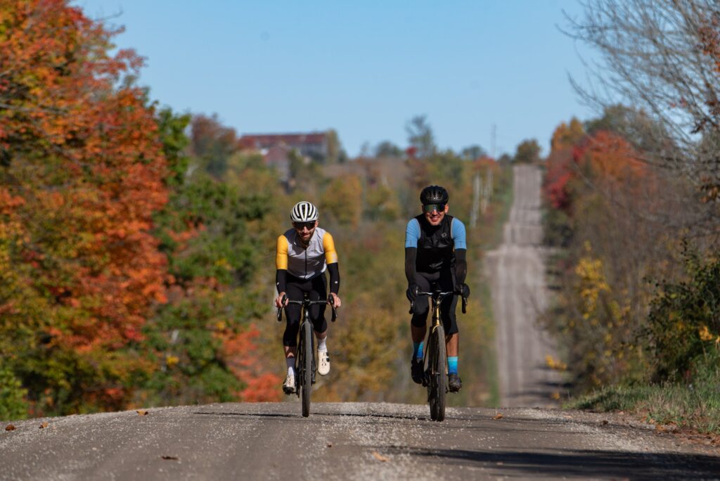 Two cyclists riding a gravel road through fall colours