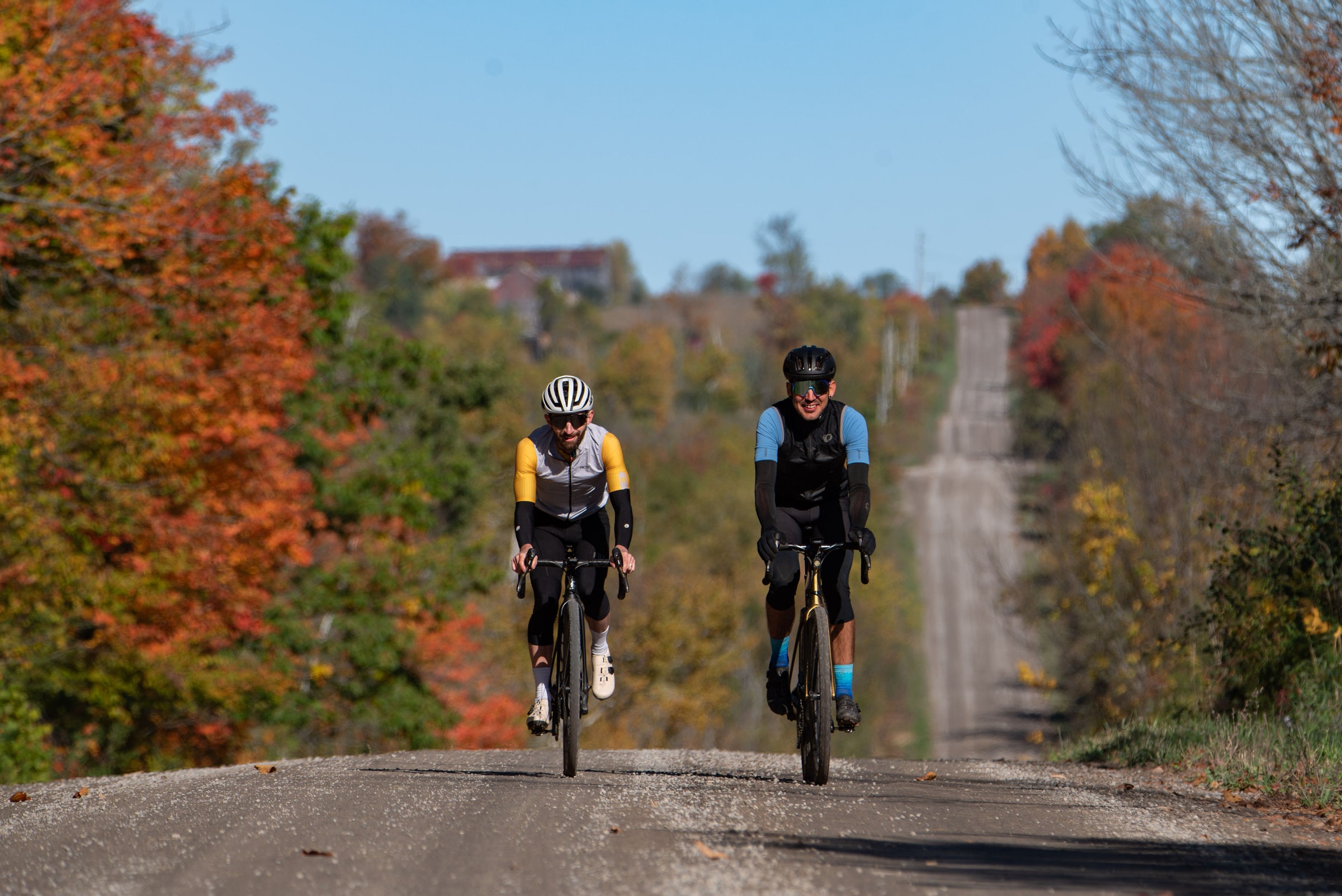 Two cyclists riding a gravel road through fall colours
