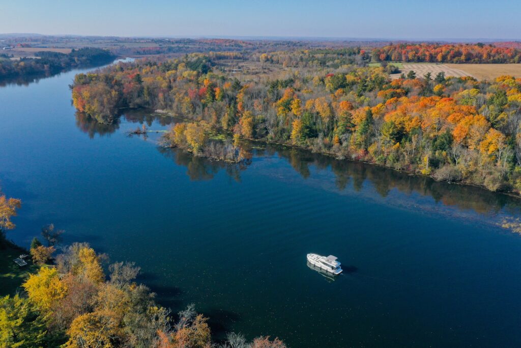 Aerial view of a boat cruising a river lined with fall colours in Kawarthas Northumberland