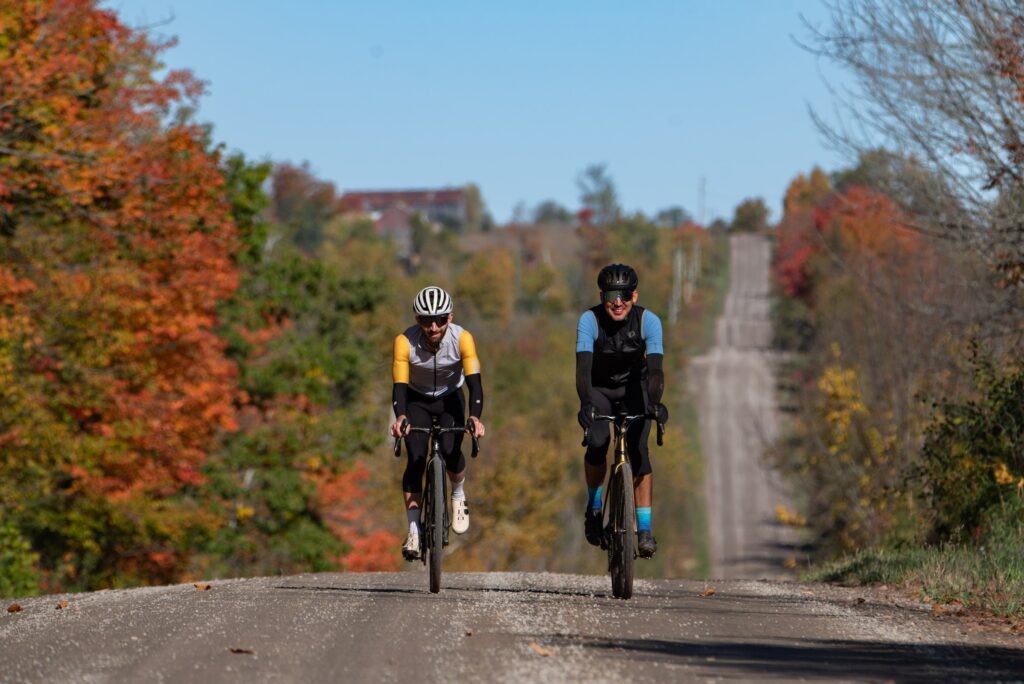 Two cyclists riding a gravel road lined with fall colours